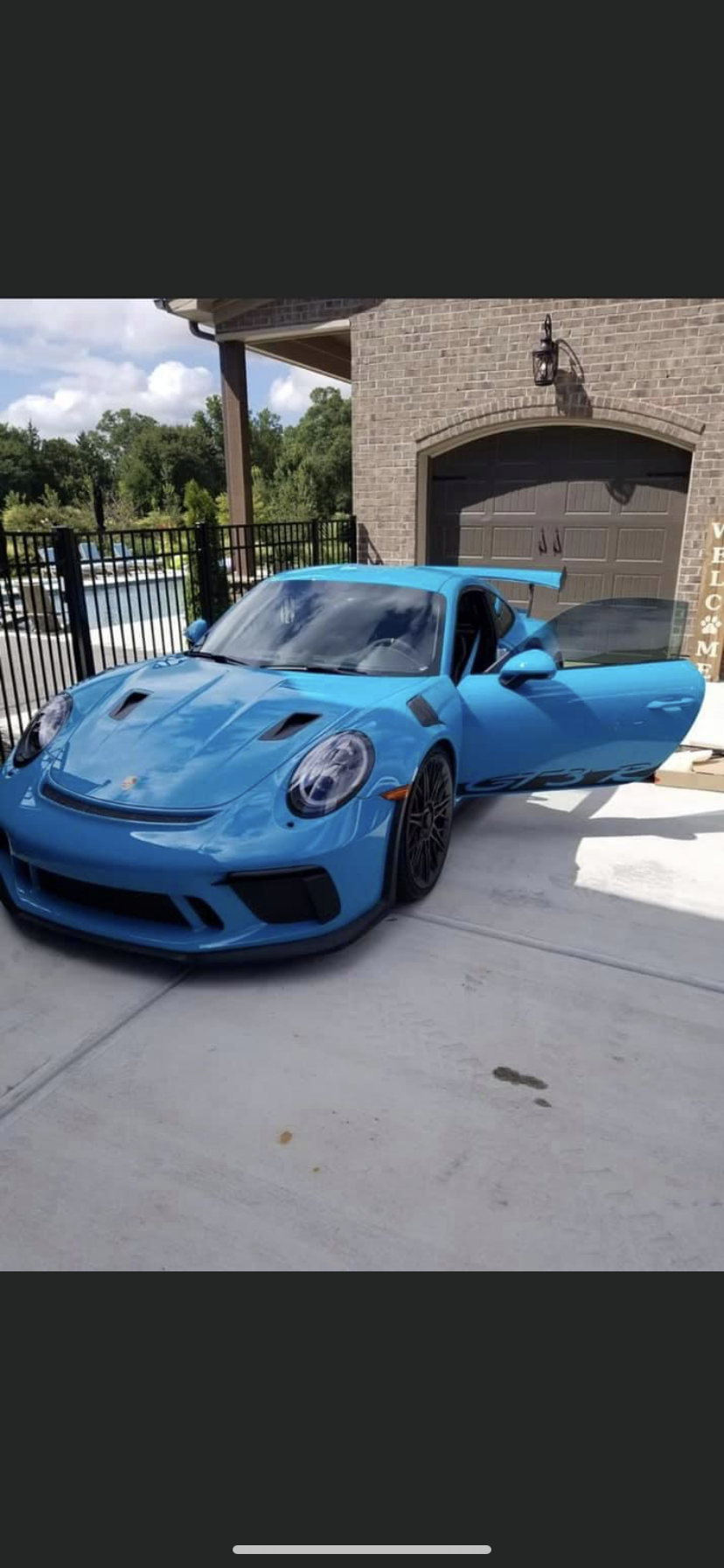 Blue Porsche 911 GT3 RS with the door open parked in front of a house.