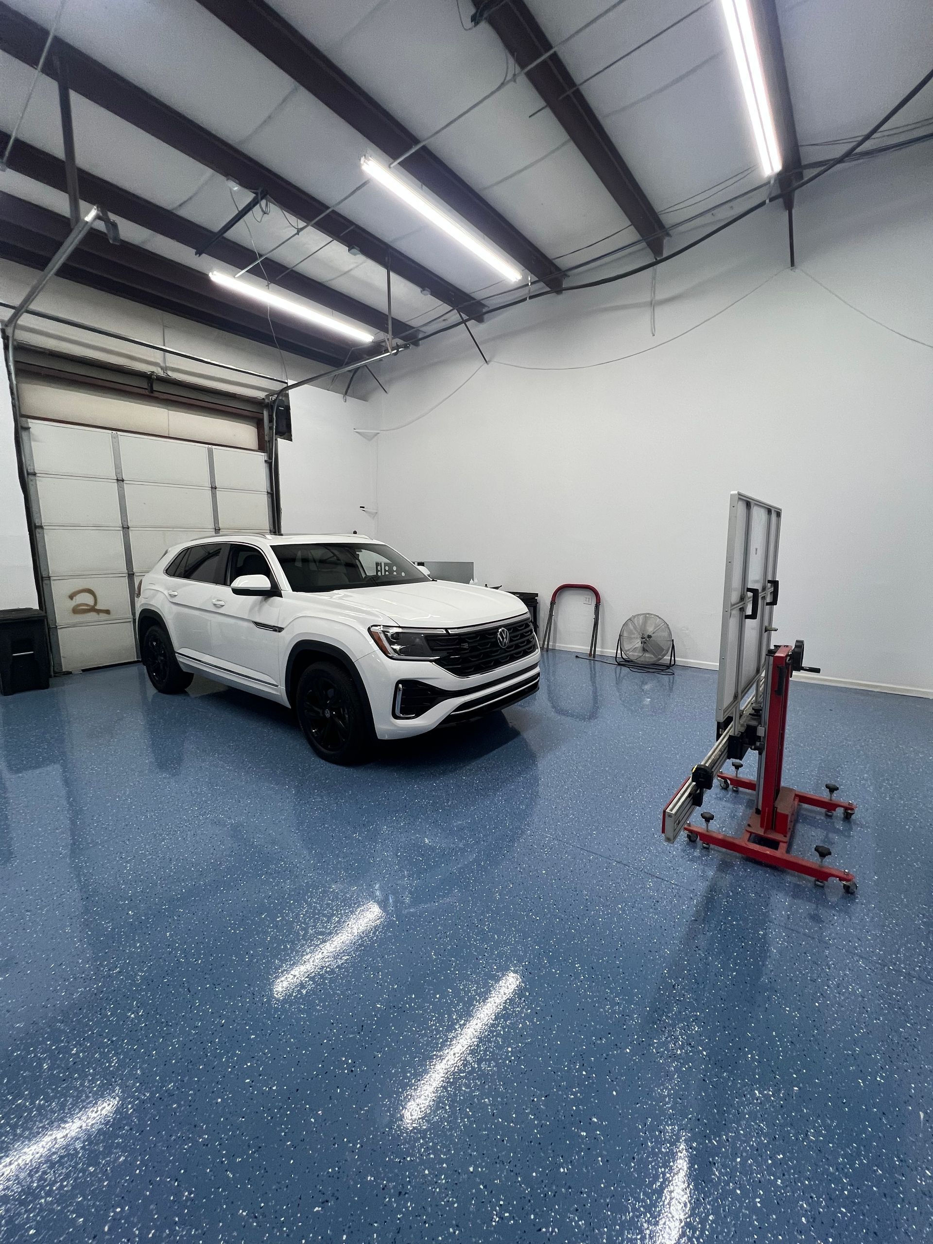 White SUV inside a repair shop, with alignment equipment in front. Blue epoxy floor, overhead lights.