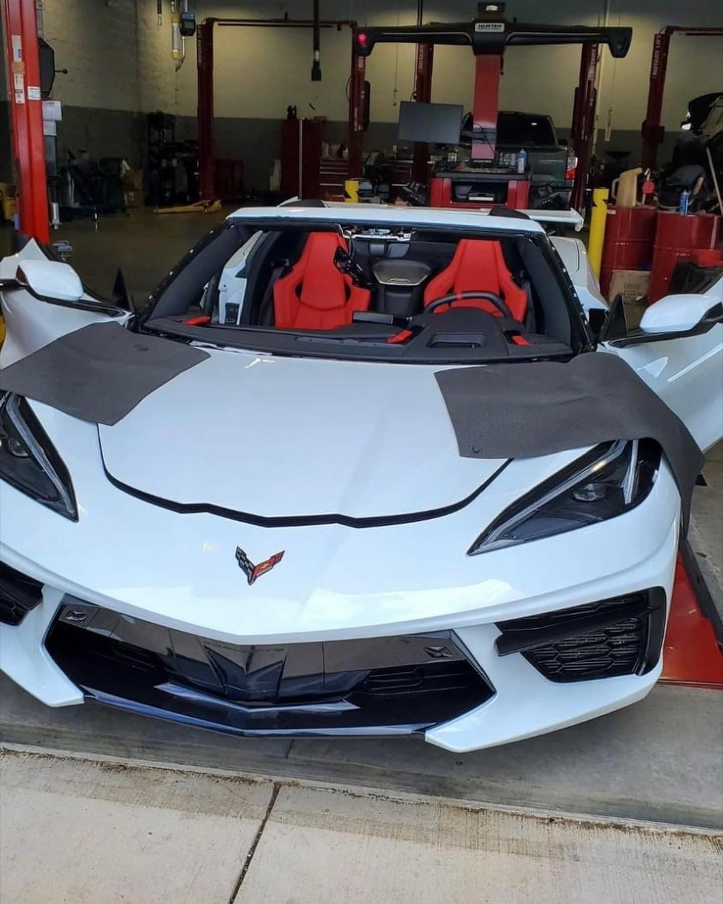 White Chevrolet Corvette in a garage with open doors and red seats.