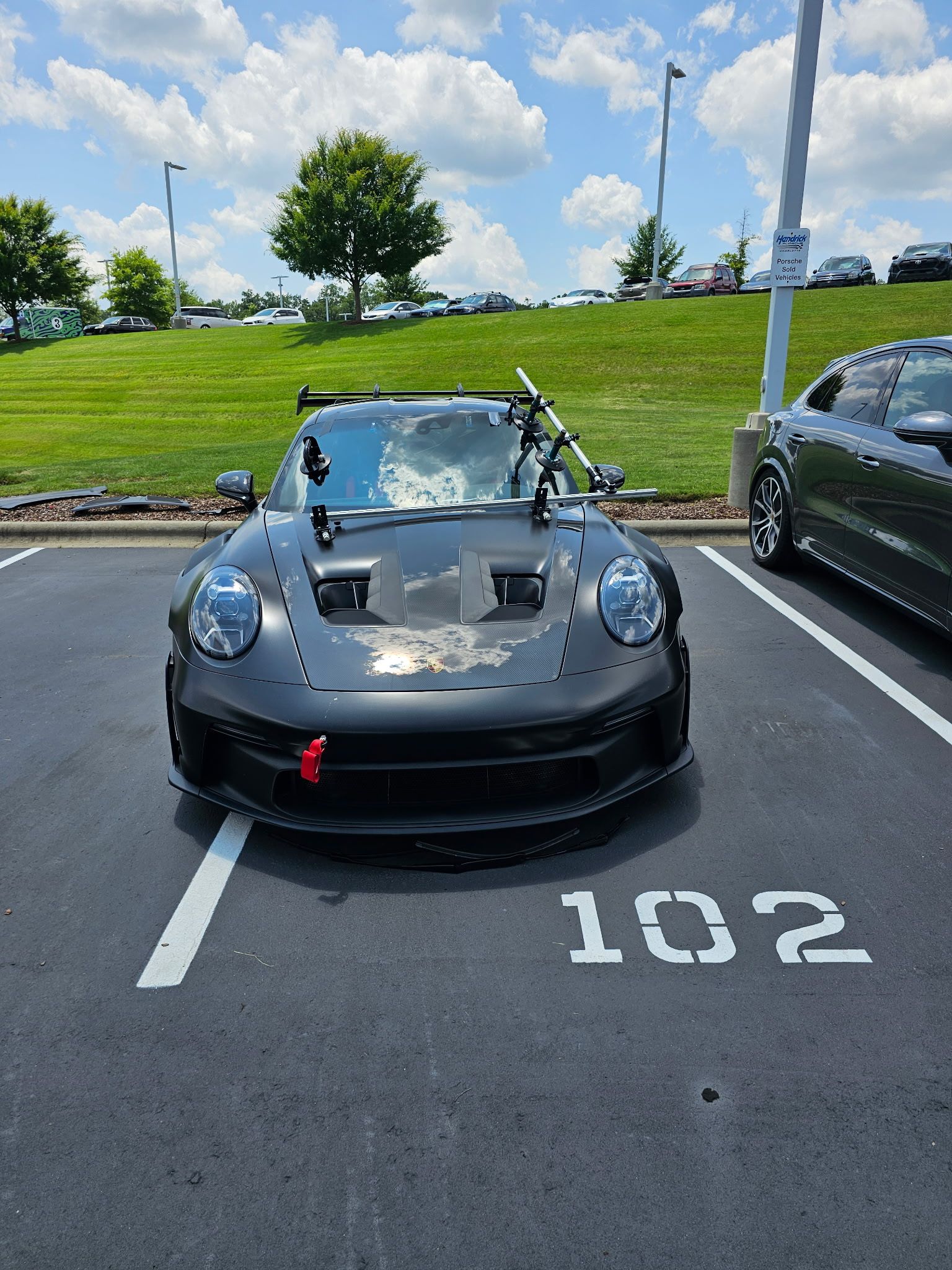 Black Porsche sports car with modifications, parked in spot 102 on a sunny day.