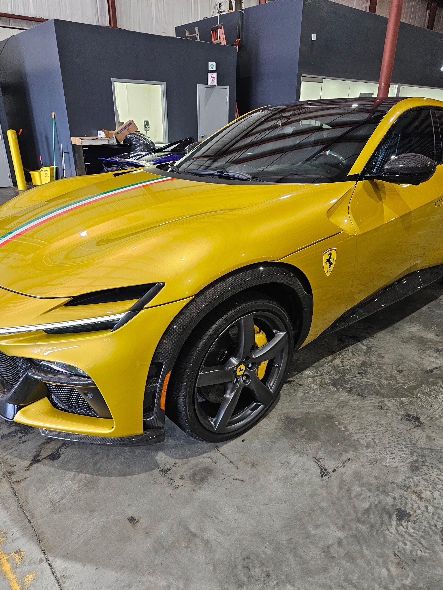 Yellow Ferrari parked indoors, green and red stripe detail, black wheels.