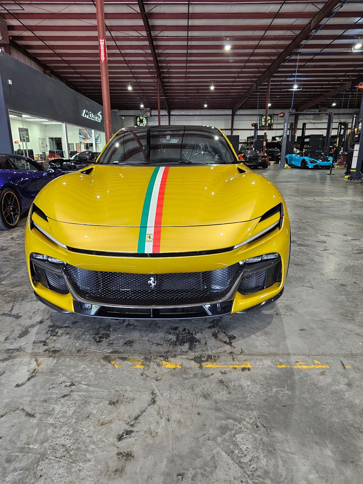 Yellow sports car with Italian flag stripes on hood inside a garage.