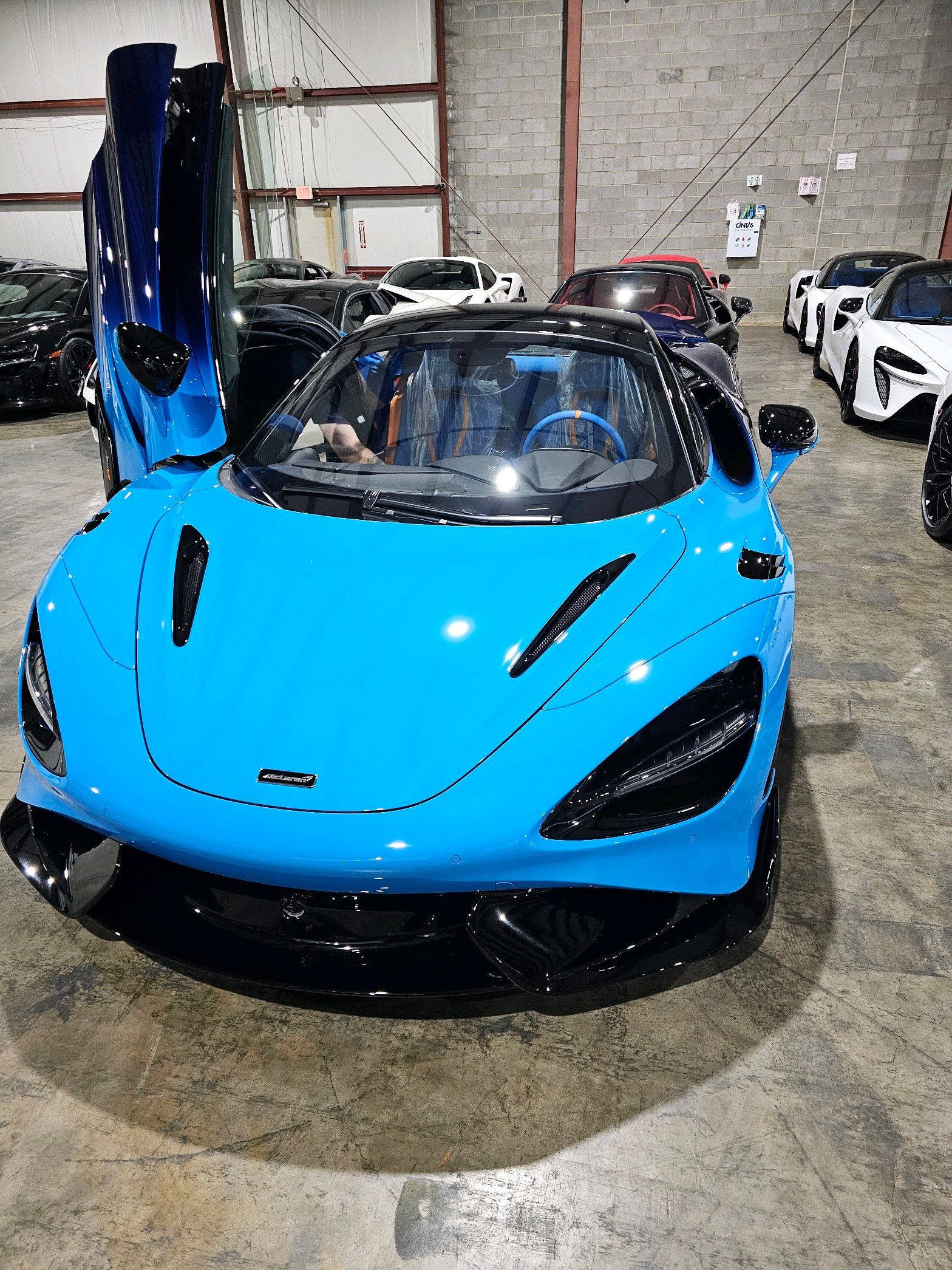 Blue McLaren sports car with open door, parked in a showroom.
