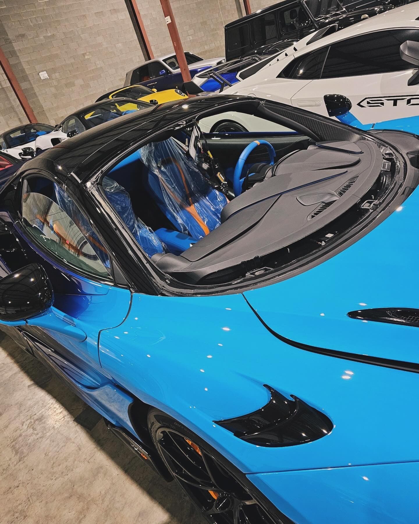 Bright blue sports car with black accents, parked in a garage with other luxury vehicles.
