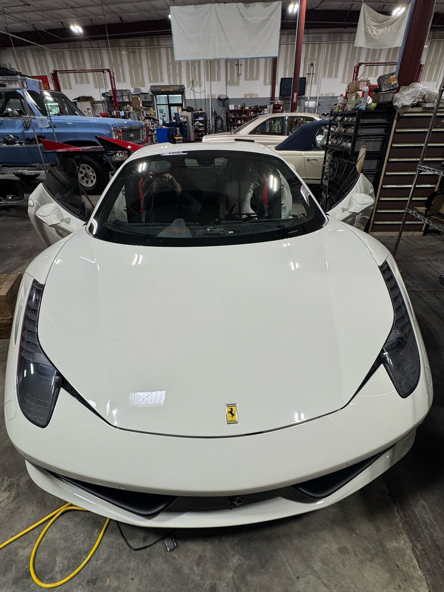 White Ferrari sports car with open doors in a repair shop.