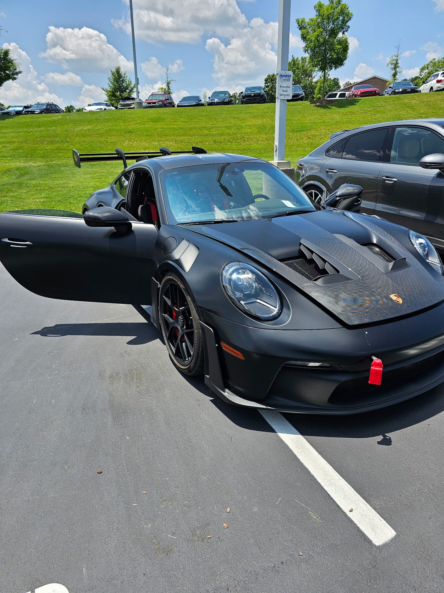 Black Porsche sports car with open door parked in a lot on a sunny day.