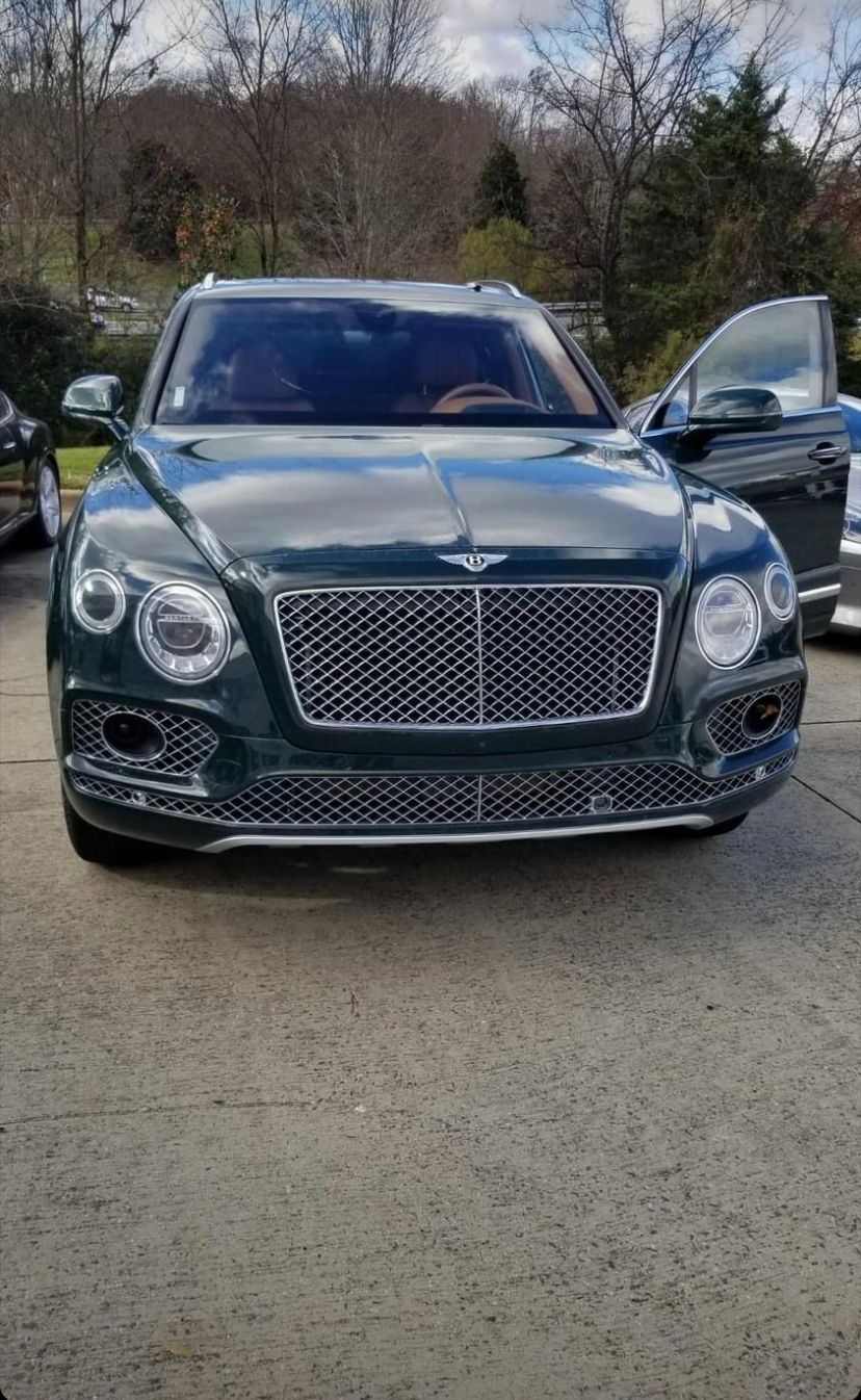 Green Bentley SUV parked outside with open door.