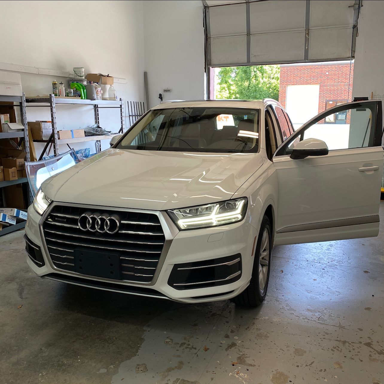 White Audi SUV with driver's side door open, parked inside a garage.
