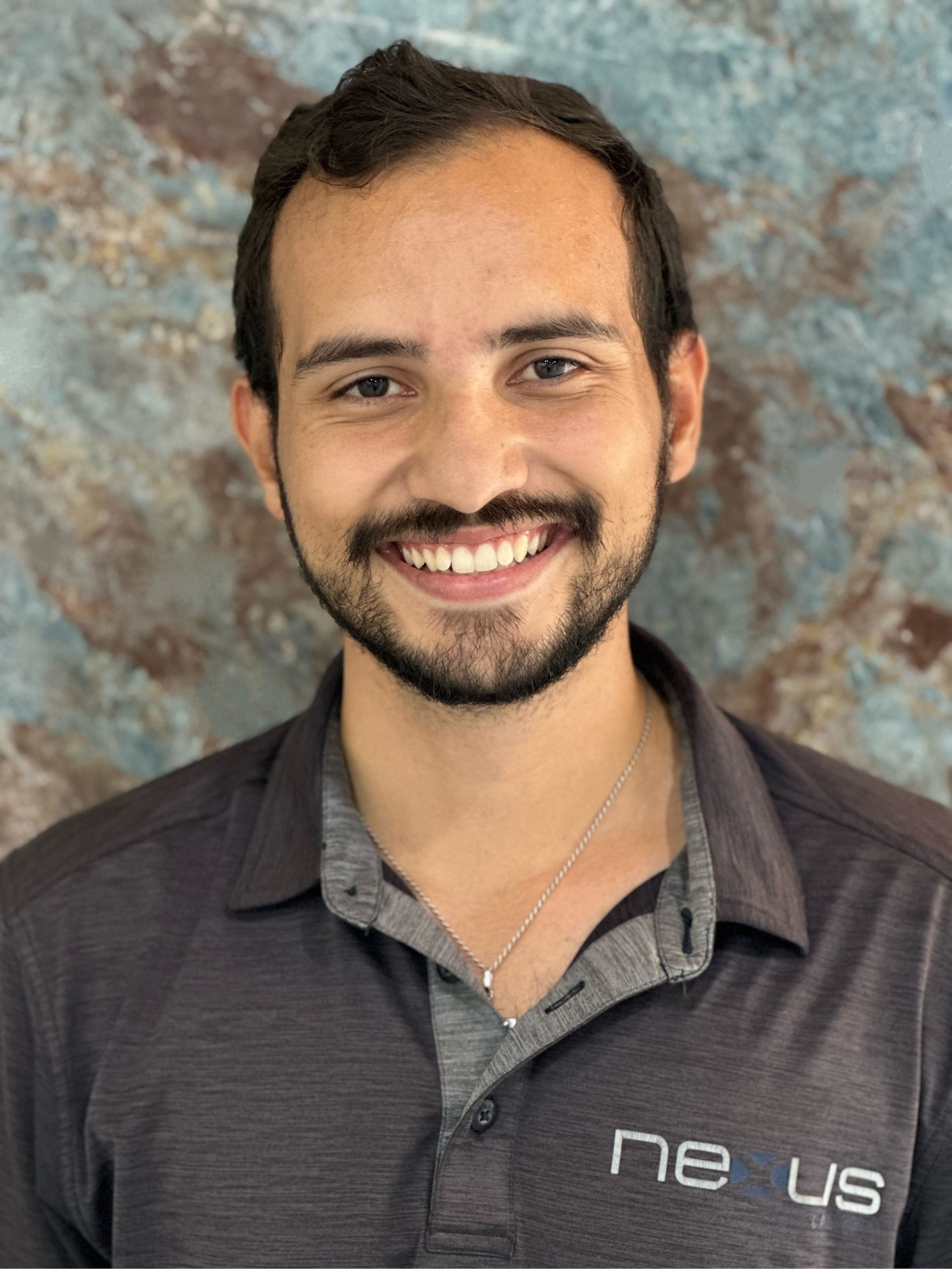 A man with a beard is smiling for the camera while wearing a polo shirt.