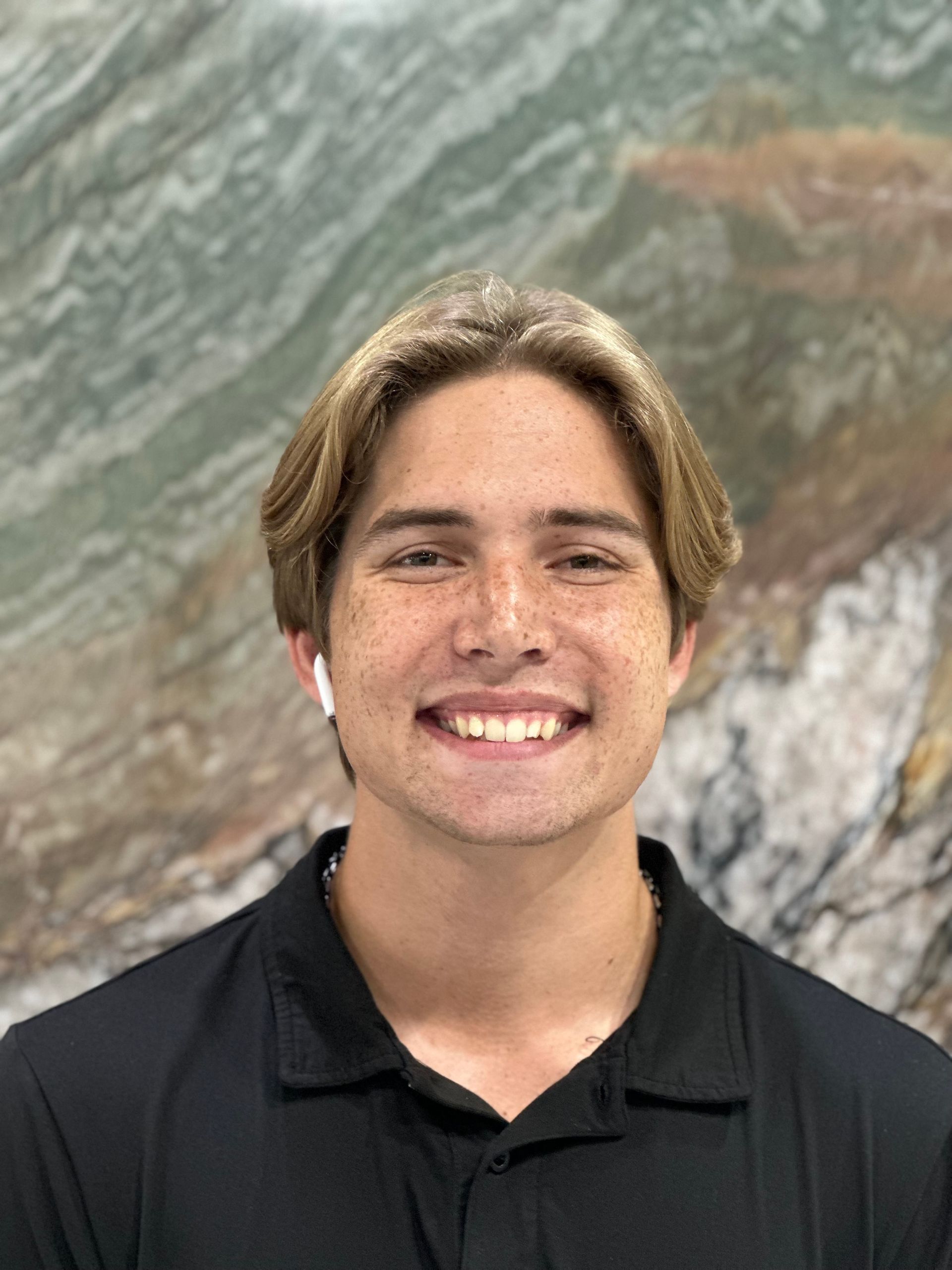 A young man in a black shirt is smiling in front of a painting.