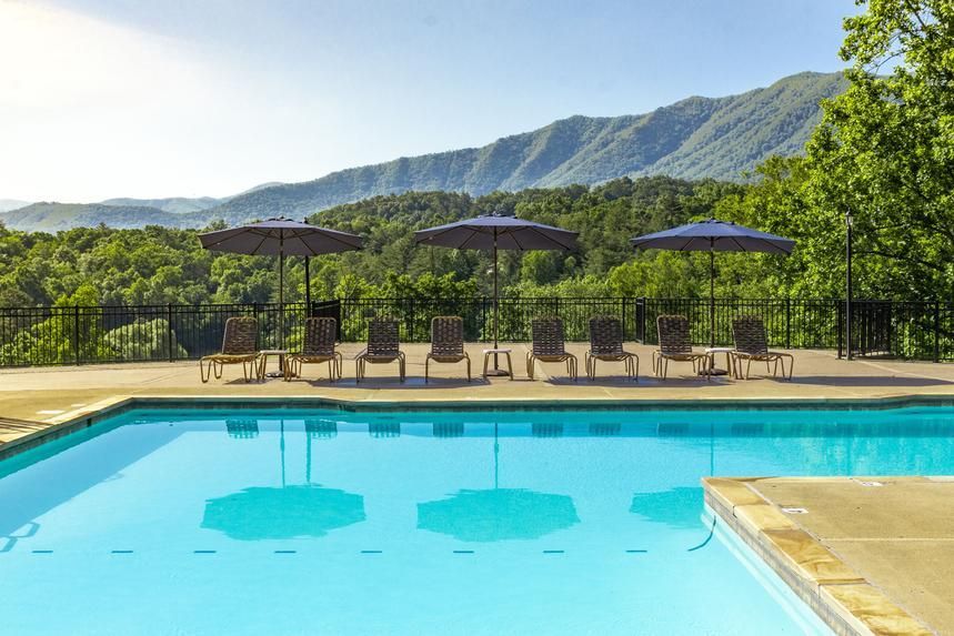 A large swimming pool surrounded by chairs and umbrellas with mountains in the background.