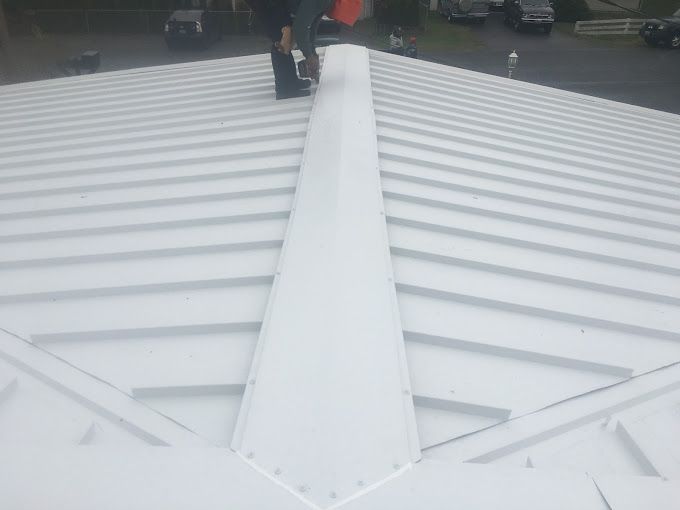 A man is standing on top of a white metal roof.