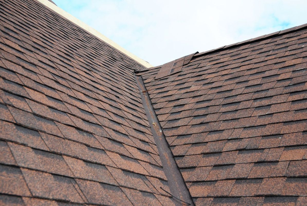 A close up of a roof with brown shingles and a blue sky in the background.