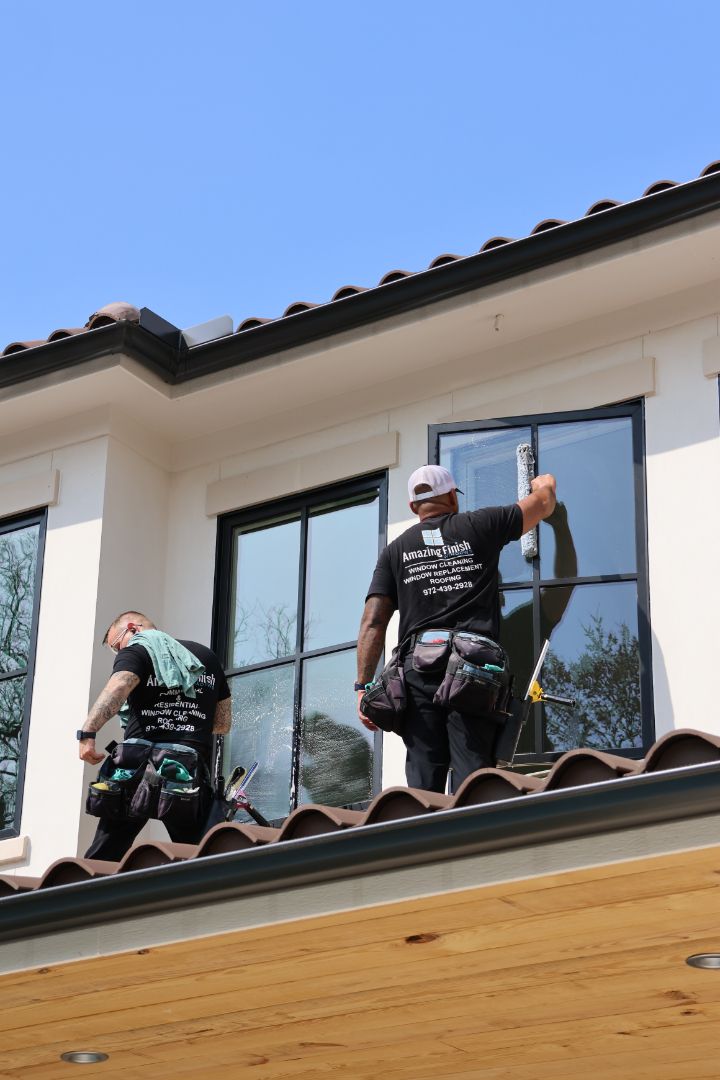 Two men are standing on the roof of a house cleaning windows.