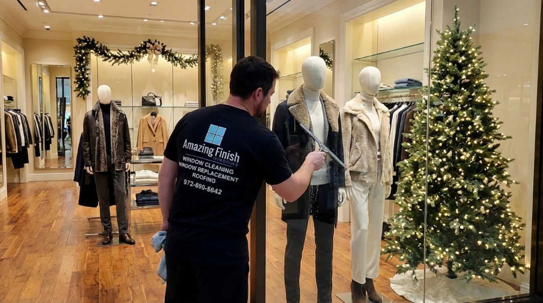 Amazing Finish Windows technician cleaning a boutique’s holiday storefront window inside a luxury retail space.