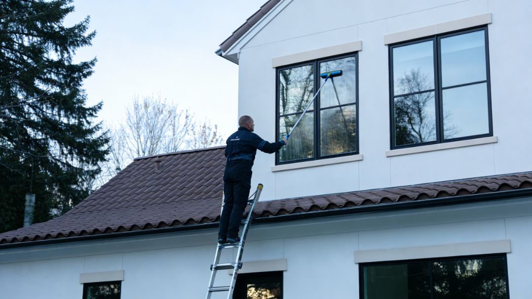 Amazing Finish Windows technician cleaning an upper exterior window on a ladder during winter.
