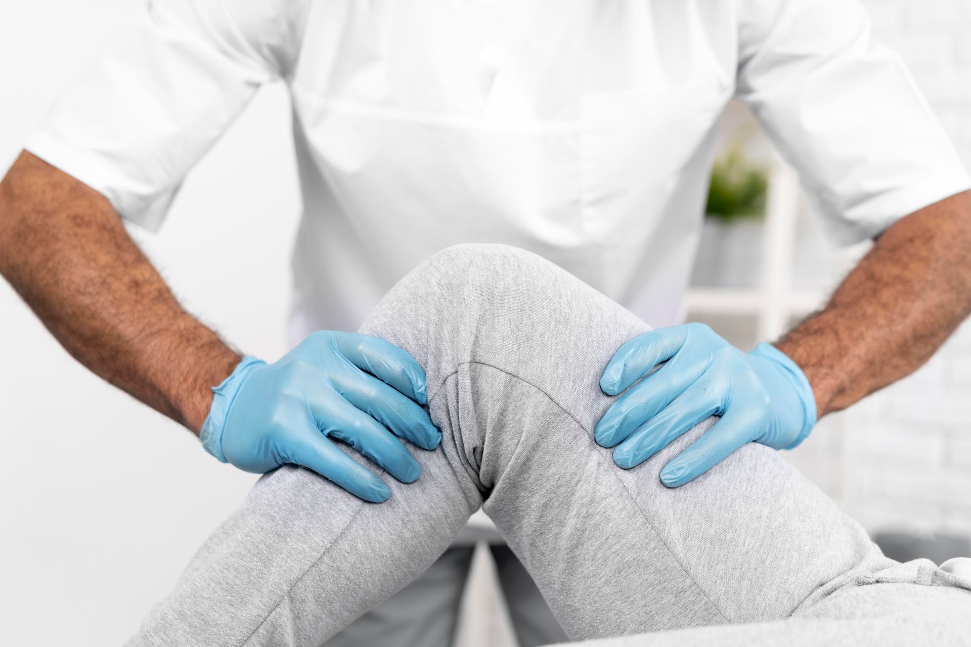 A doctor is examining a patient 's knee while wearing blue gloves.