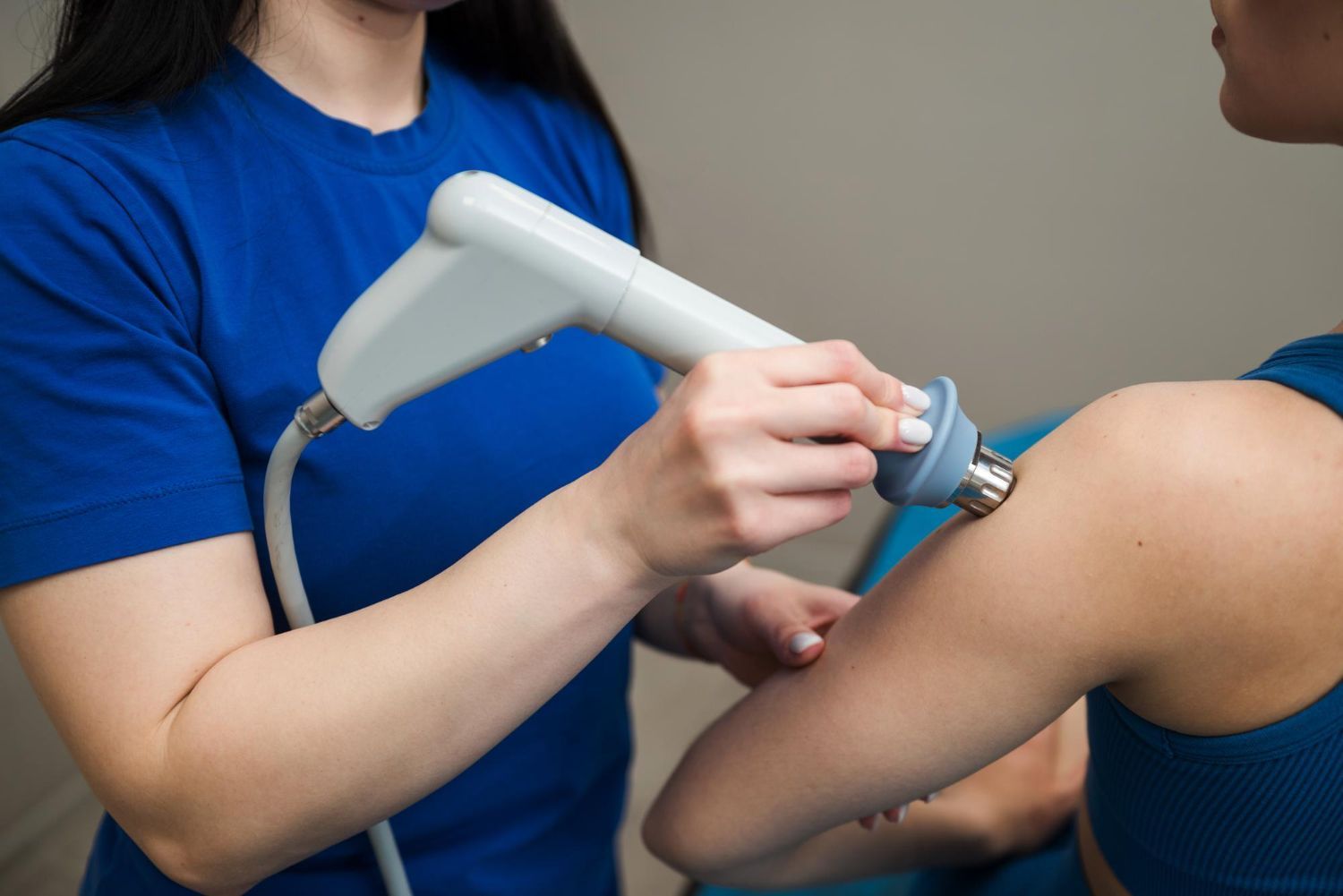 A woman is using a machine on a patient 's shoulder.