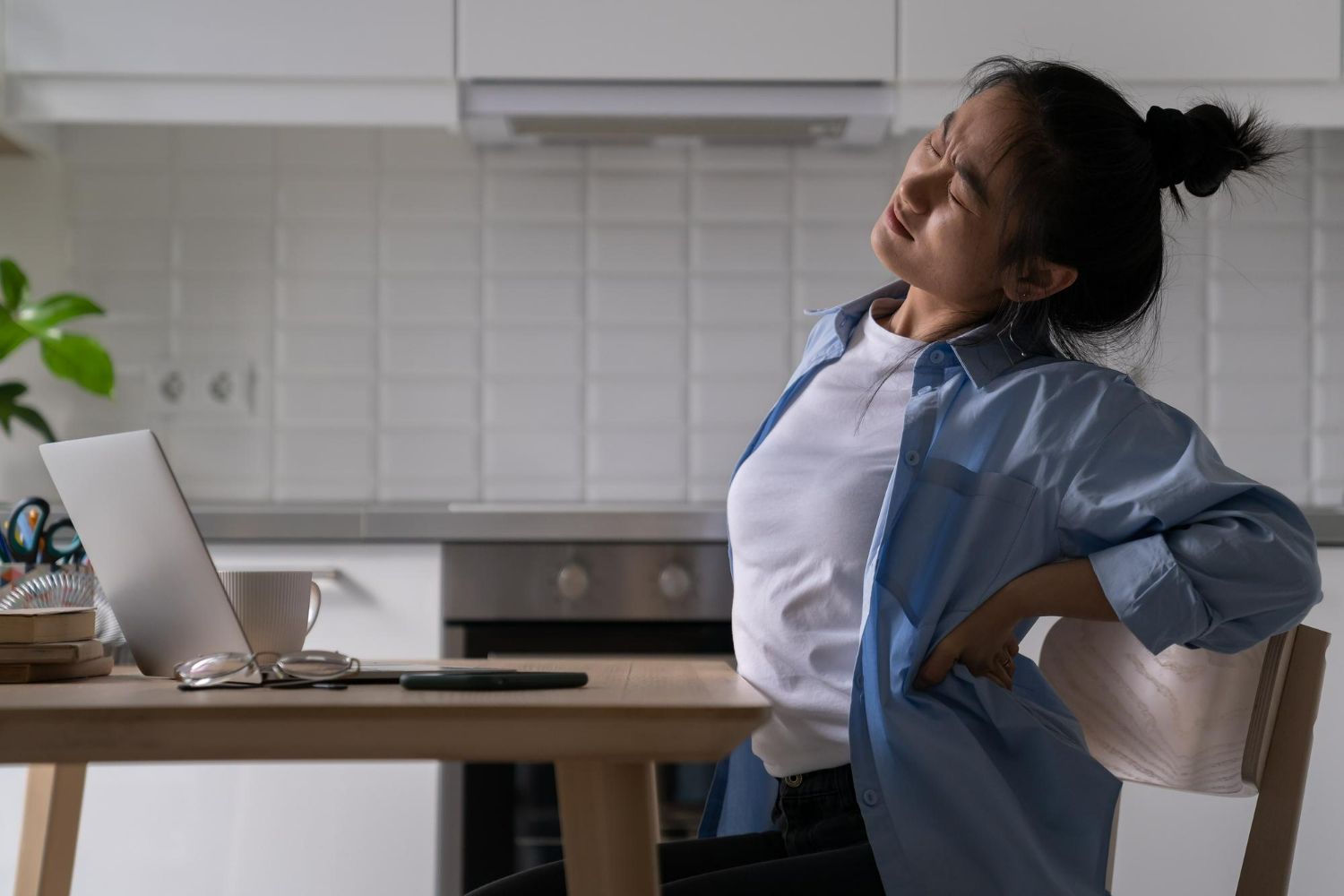 A woman is sitting at a desk with her back in pain.