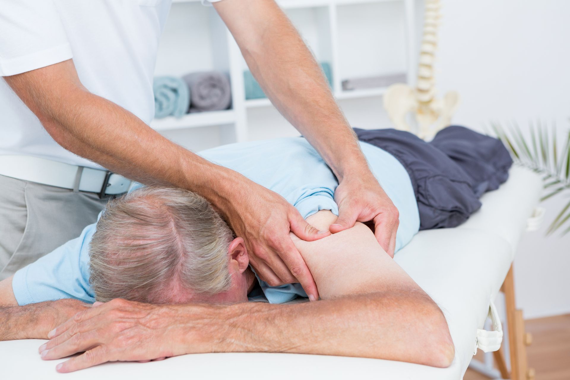 Man receiving shoulder massage from a therapist. Clinic setting, neutral colors.