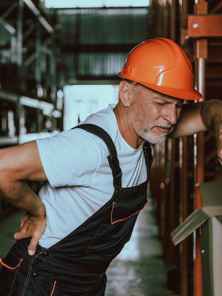 a man wearing an orange hard hat is holding his back in pain .