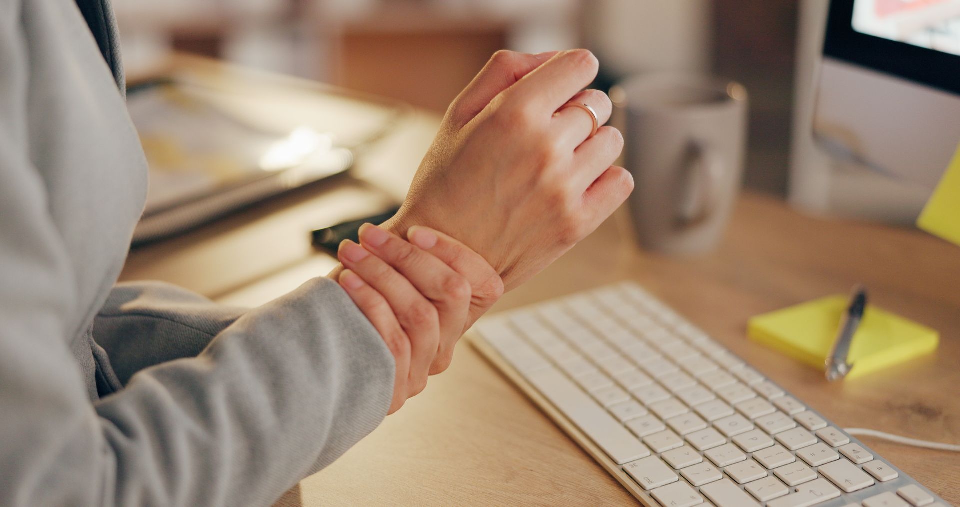 Person at desk holding wrist, possibly in pain, near a keyboard.