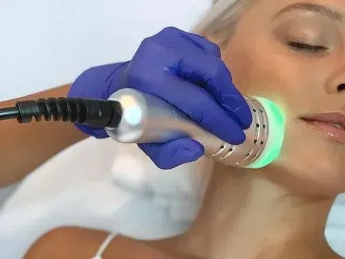 Person receiving a facial treatment with a device emitting green light on their cheek.