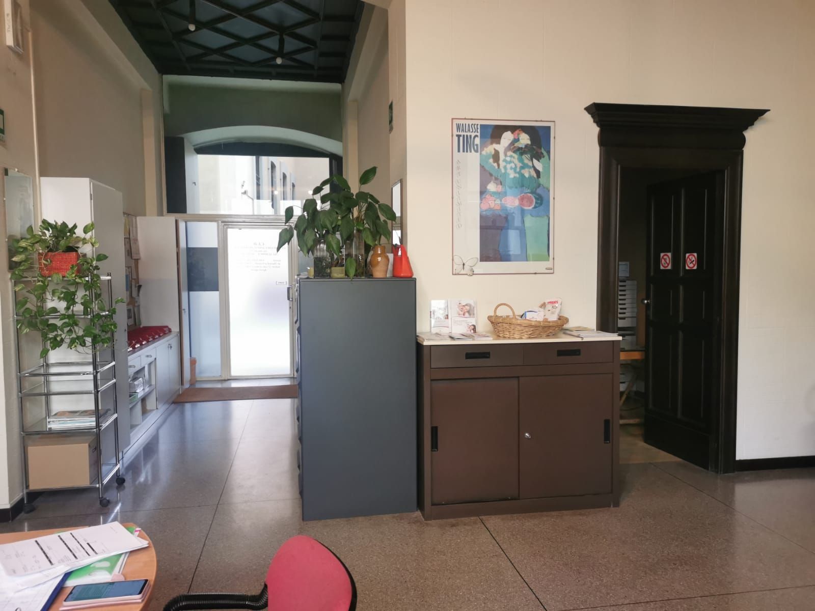 Corridoio interno con scrivania, armadio e porta scura, pareti chiare e un poster.