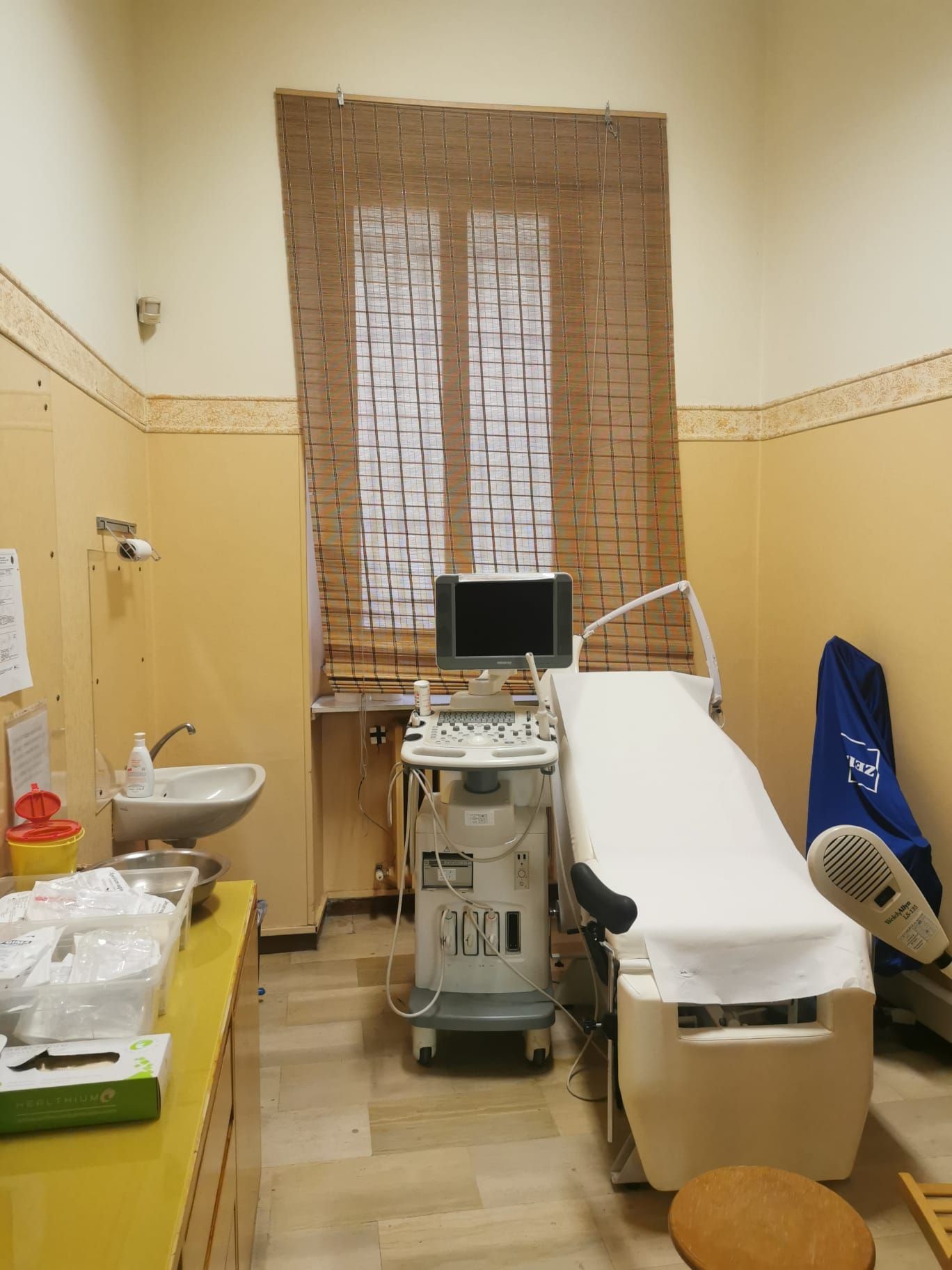 Sala visite mediche con ecografo, lettino per visite e lavandino.