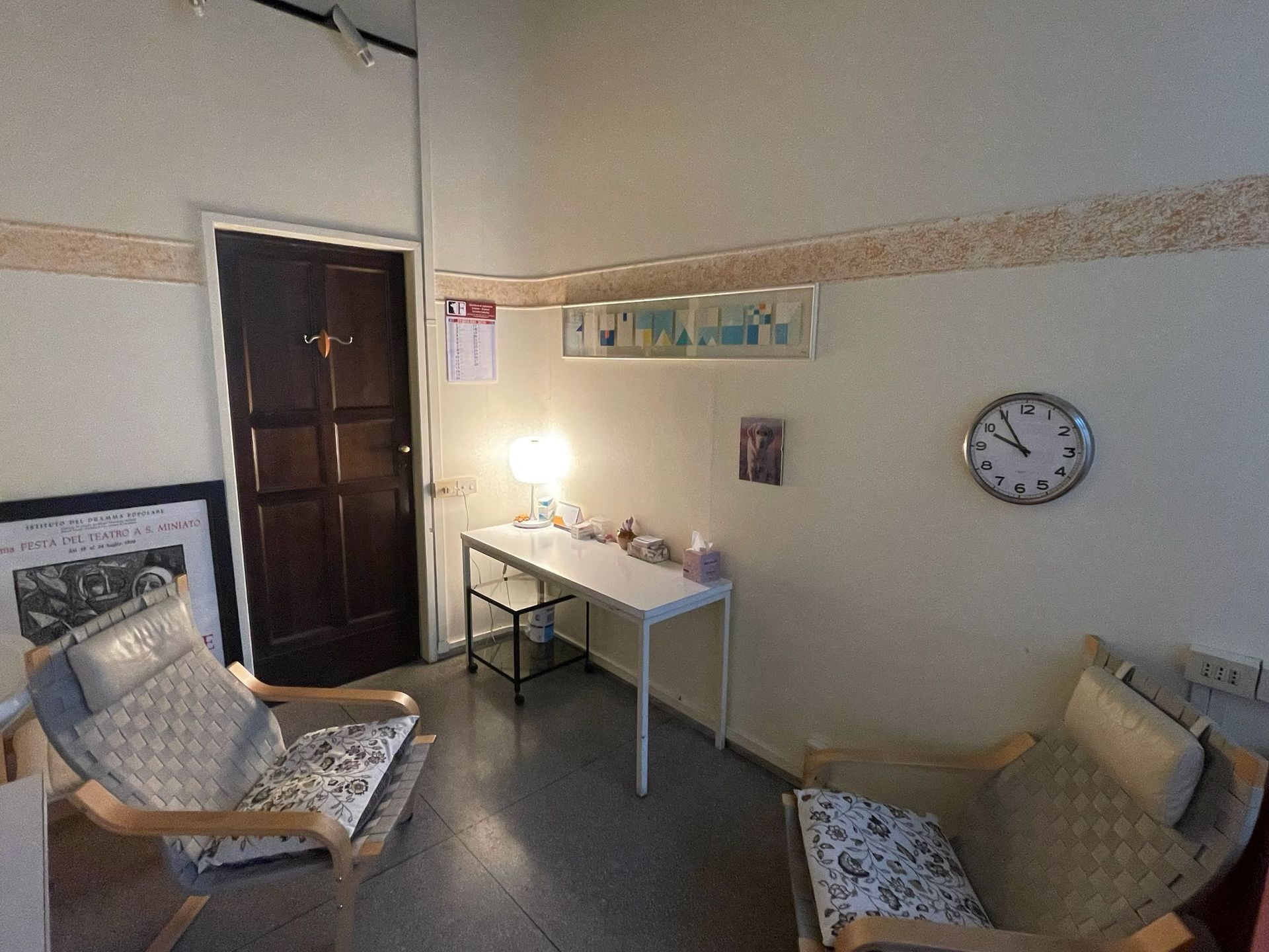 Stanza accogliente e rotonda con una scrivania, due poltrone, un orologio e una porta di legno scuro.