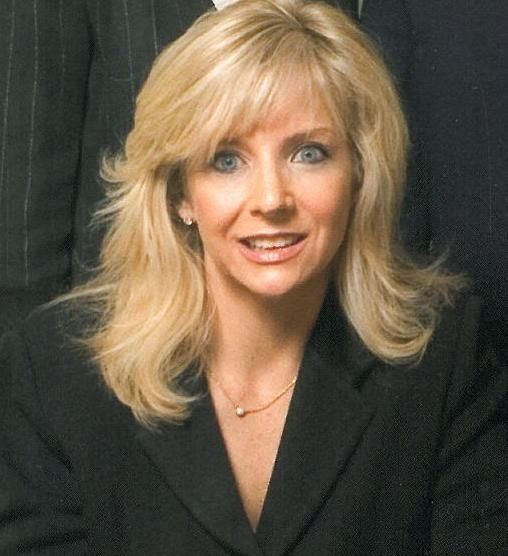 A woman in a black jacket and necklace smiles for the camera