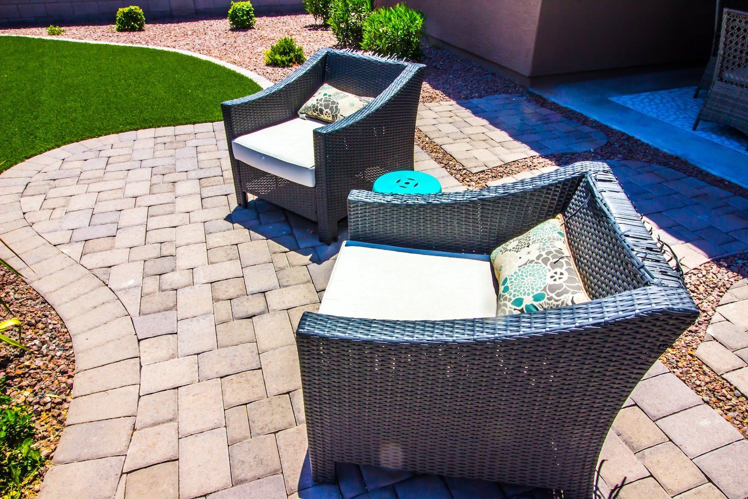 Two wicker patio chairs with comfortable cushions placed on outdoor pavers, creating an inviting outdoor seating area.