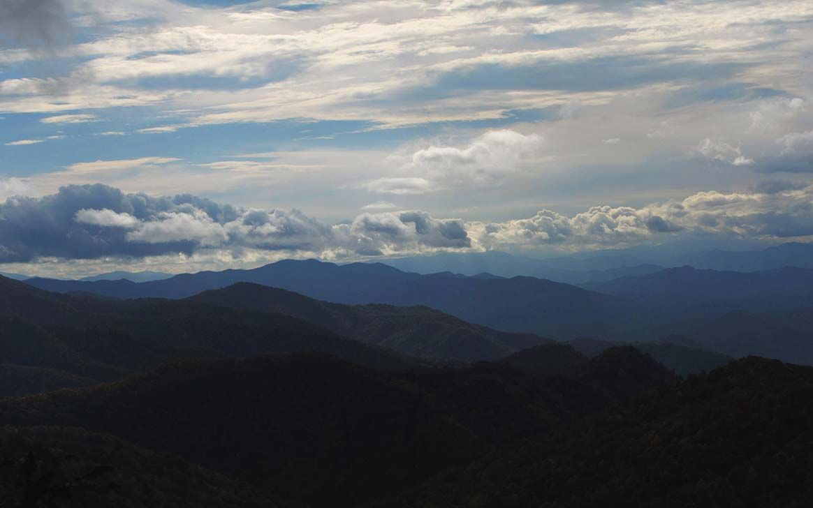 A cloudy sky over a mountain range with trees in the foreground