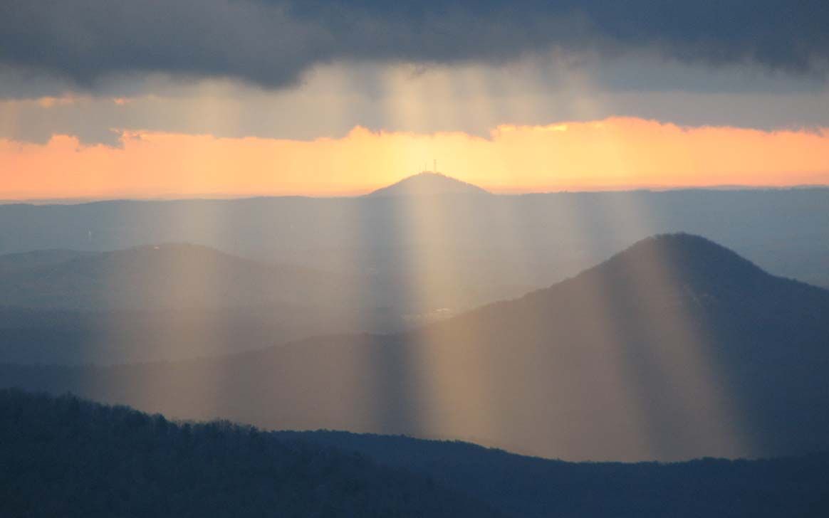 The sun is shining through the clouds over the mountains at sunset.