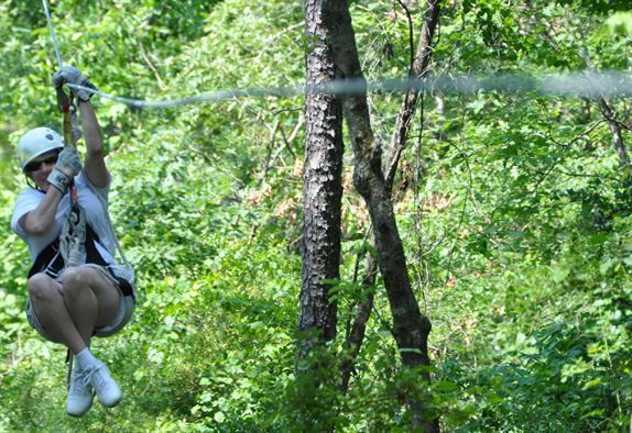 A man is flying through the air on a zip line in the woods.