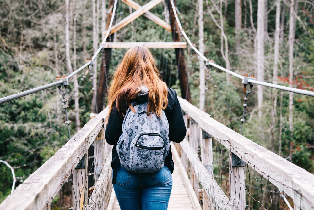 A woman with a backpack is walking across a wooden bridge.