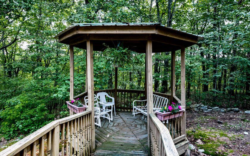 A wooden gazebo with chairs and a bench in the middle of a forest.