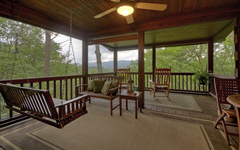 A porch with a swing and rocking chairs and a ceiling fan