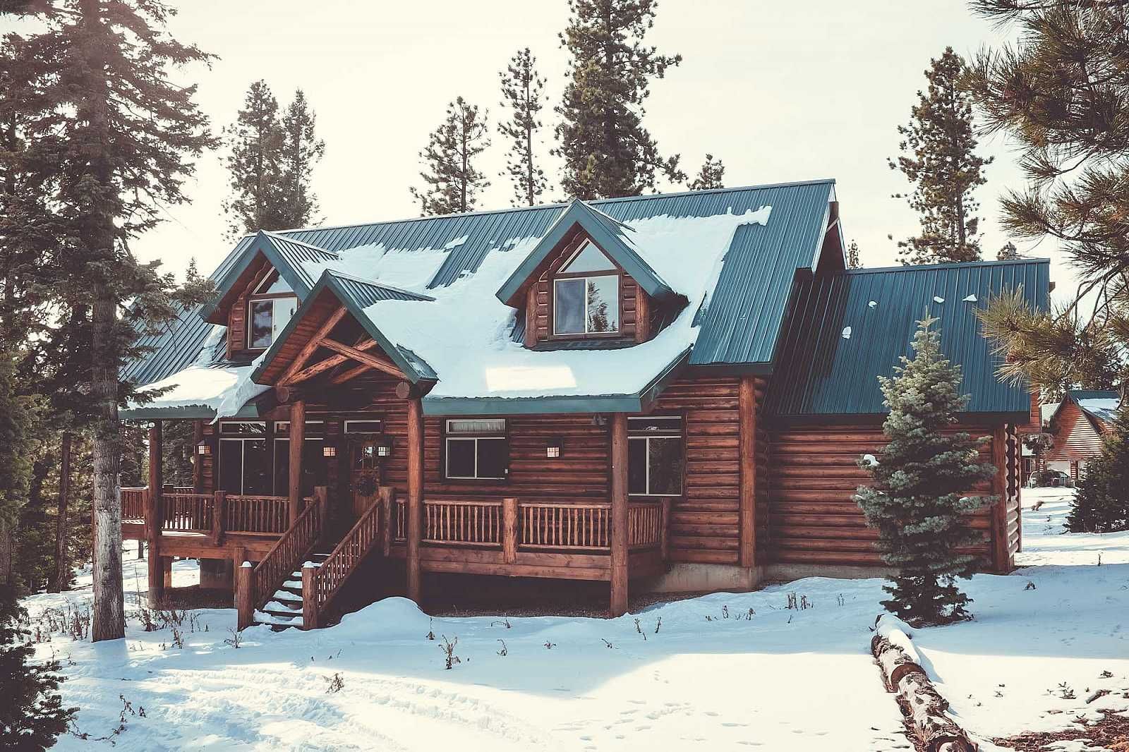 A large log cabin is surrounded by snow and trees
