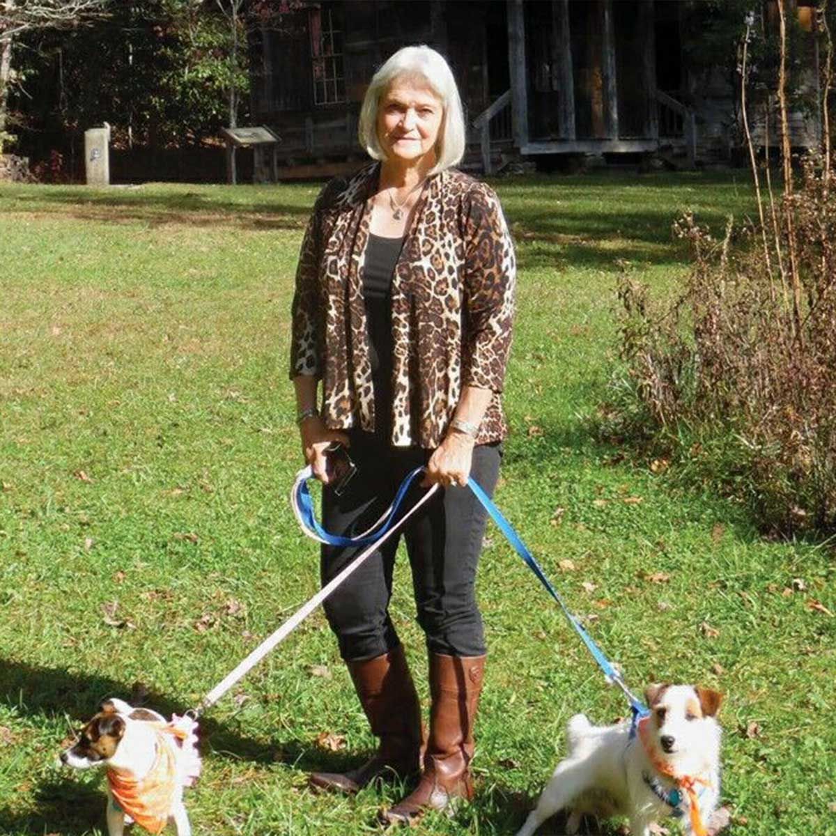 A woman in a leopard print jacket is walking two dogs on leashes
