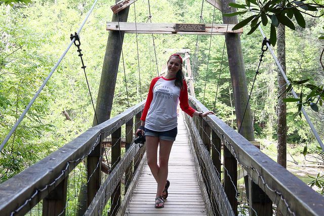 A woman is standing on a wooden bridge with trees in the background