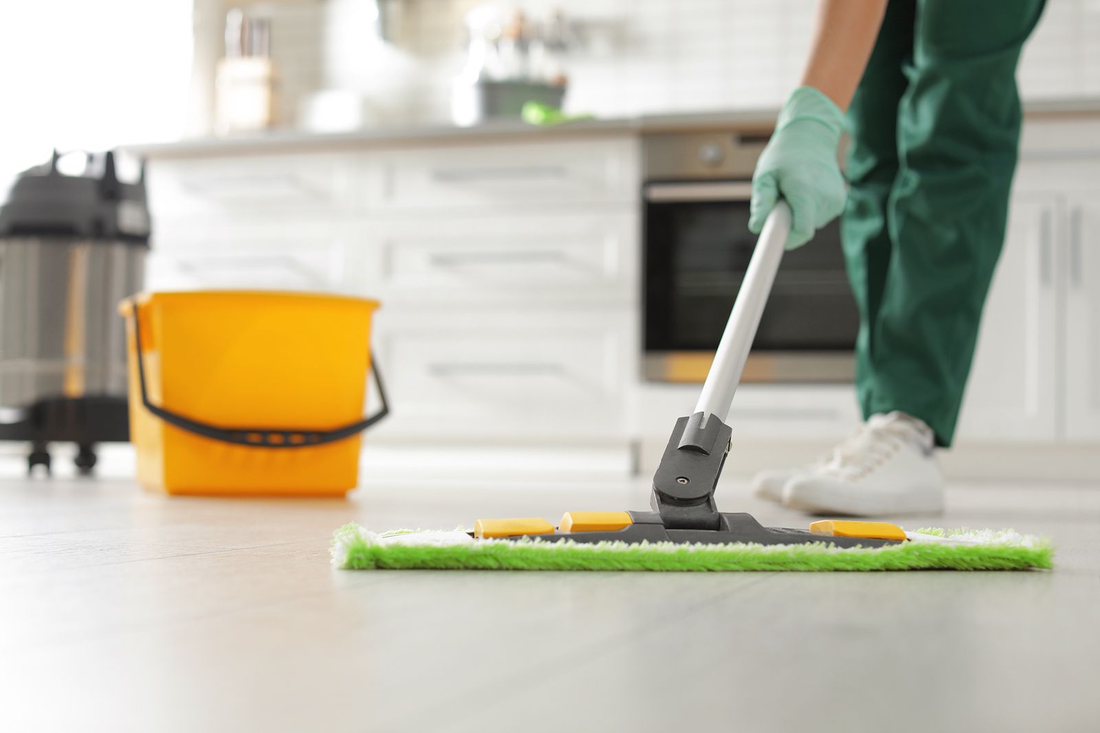 A person is cleaning the floor with a mop in a kitchen.