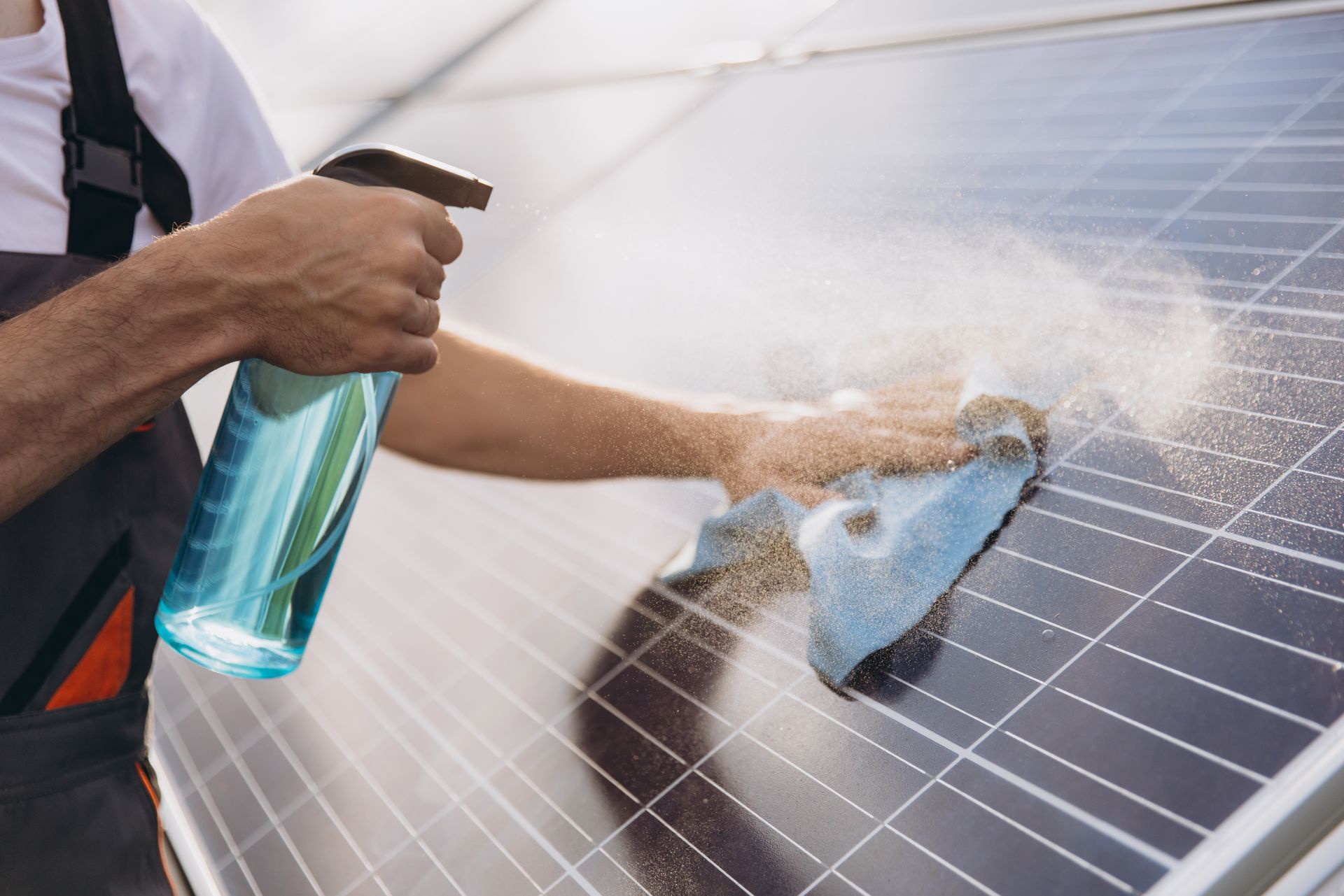 Person cleaning solar panels with spray bottle and cloth.