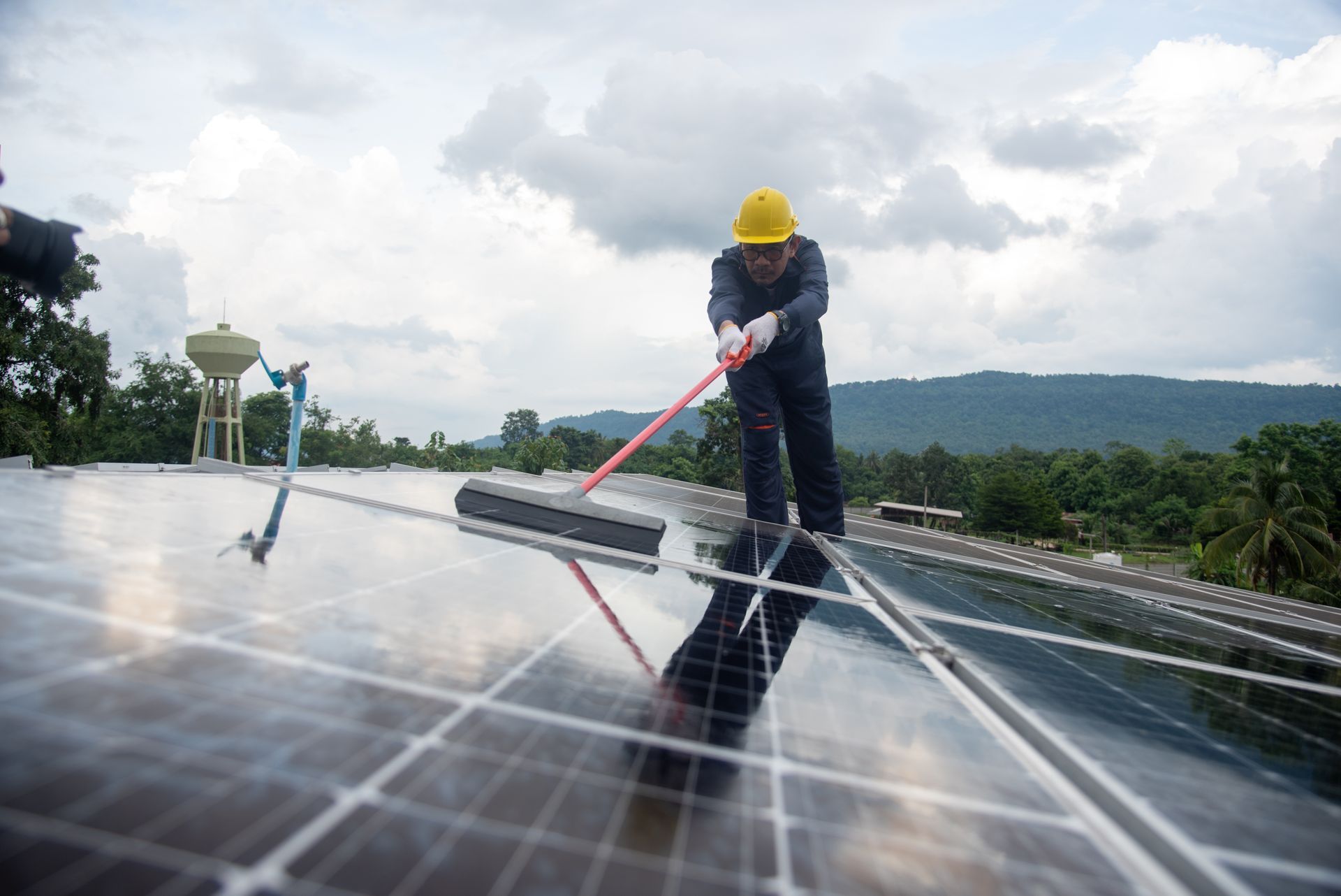 Person in yellow helmet cleaning solar panels on a roof.