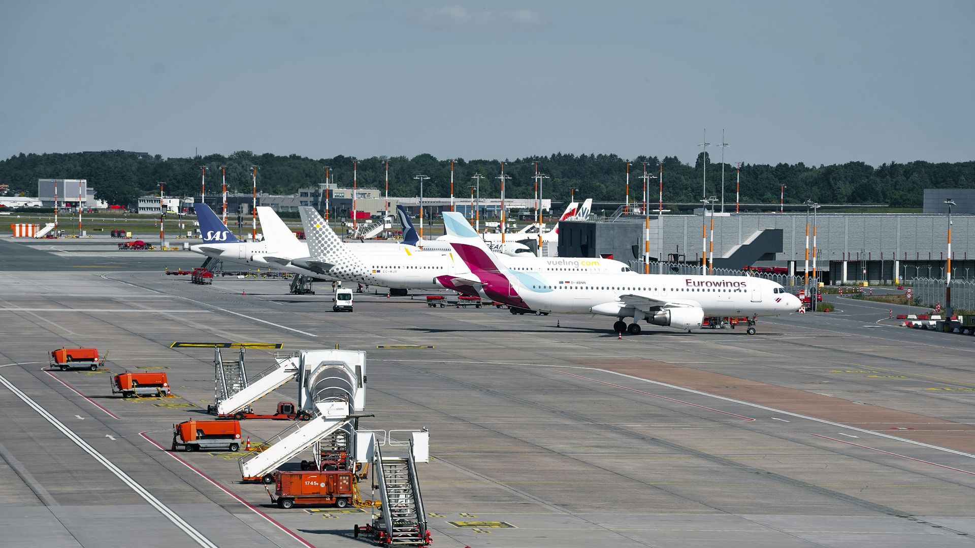 Aviones estacionados en un aeropuerto, varios con pasarelas de embarque. Asfalto gris, cielo azul.