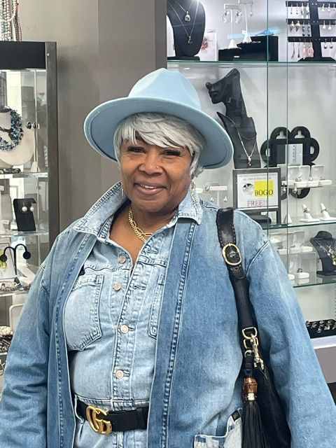 A woman wearing a blue hat and a denim jacket is standing in a store.