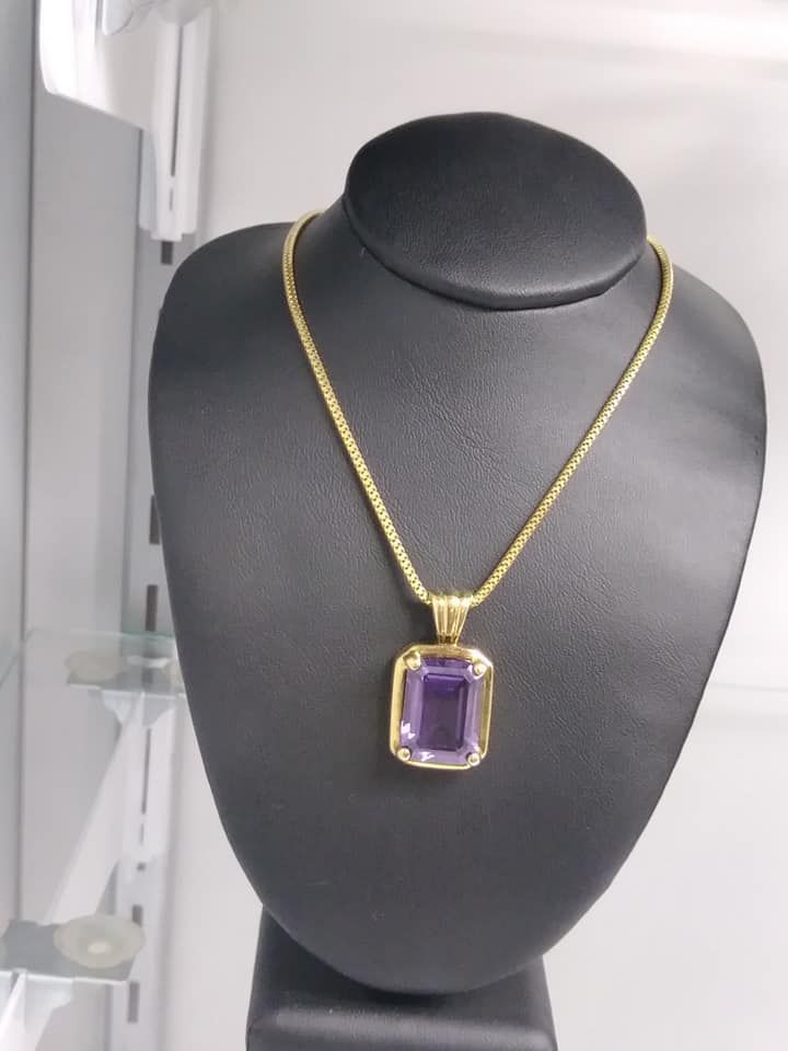 Gold necklace with a rectangular amethyst pendant on a black jewelry bust.