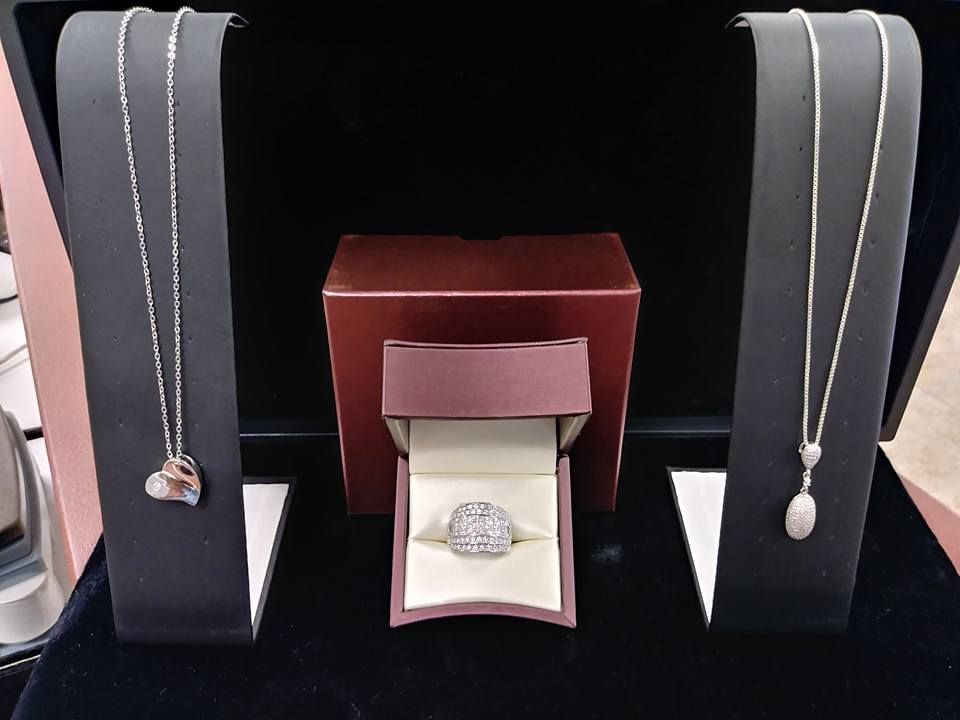 Jewelry display: necklaces on stands flanking a ring in a box, all on a dark velvet surface.