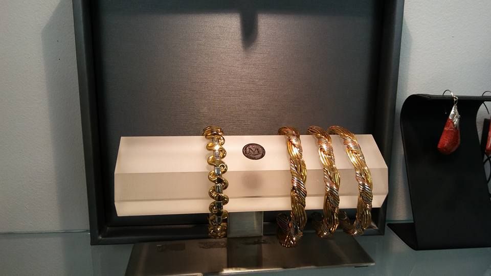 Gold bracelets on a white box inside a display case with a black backdrop, earrings to the right.