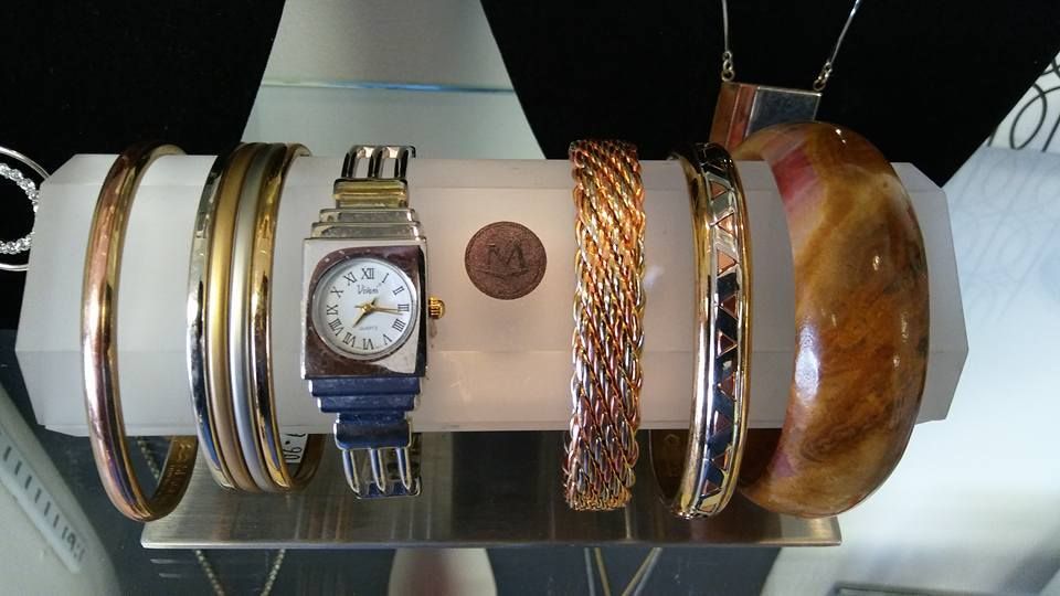 Jewelry display case with multiple bracelets and a wristwatch. Various metals and wood bangle shown on a white cylinder.